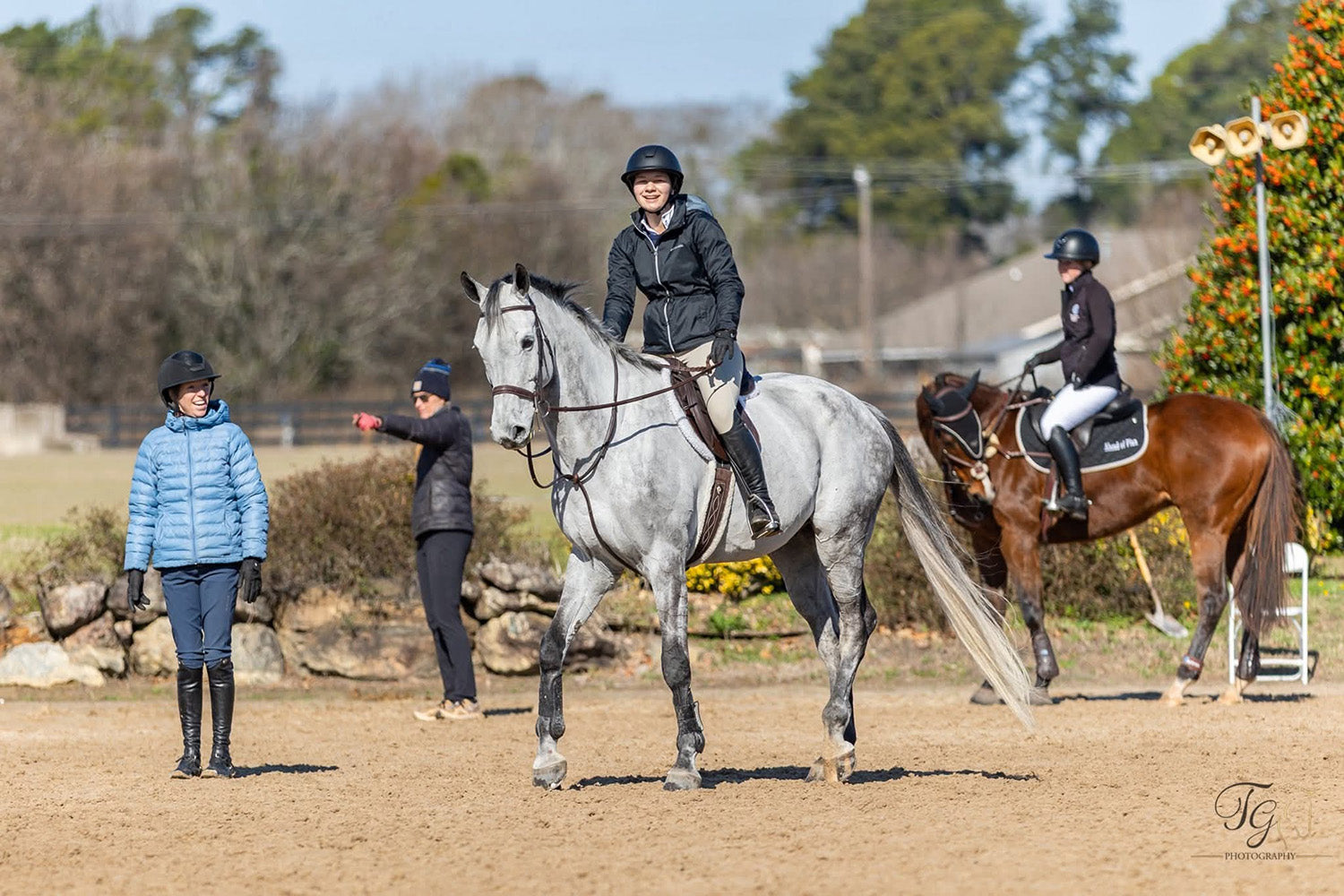 Two people riding horses in an outdoor equestrian setting with a clear sky.